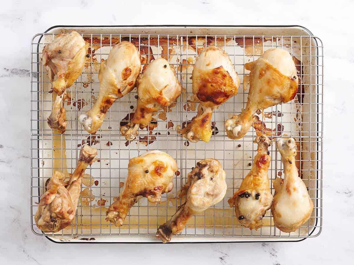 Baked chicken drumsticks on a wire rack over and baking tray.