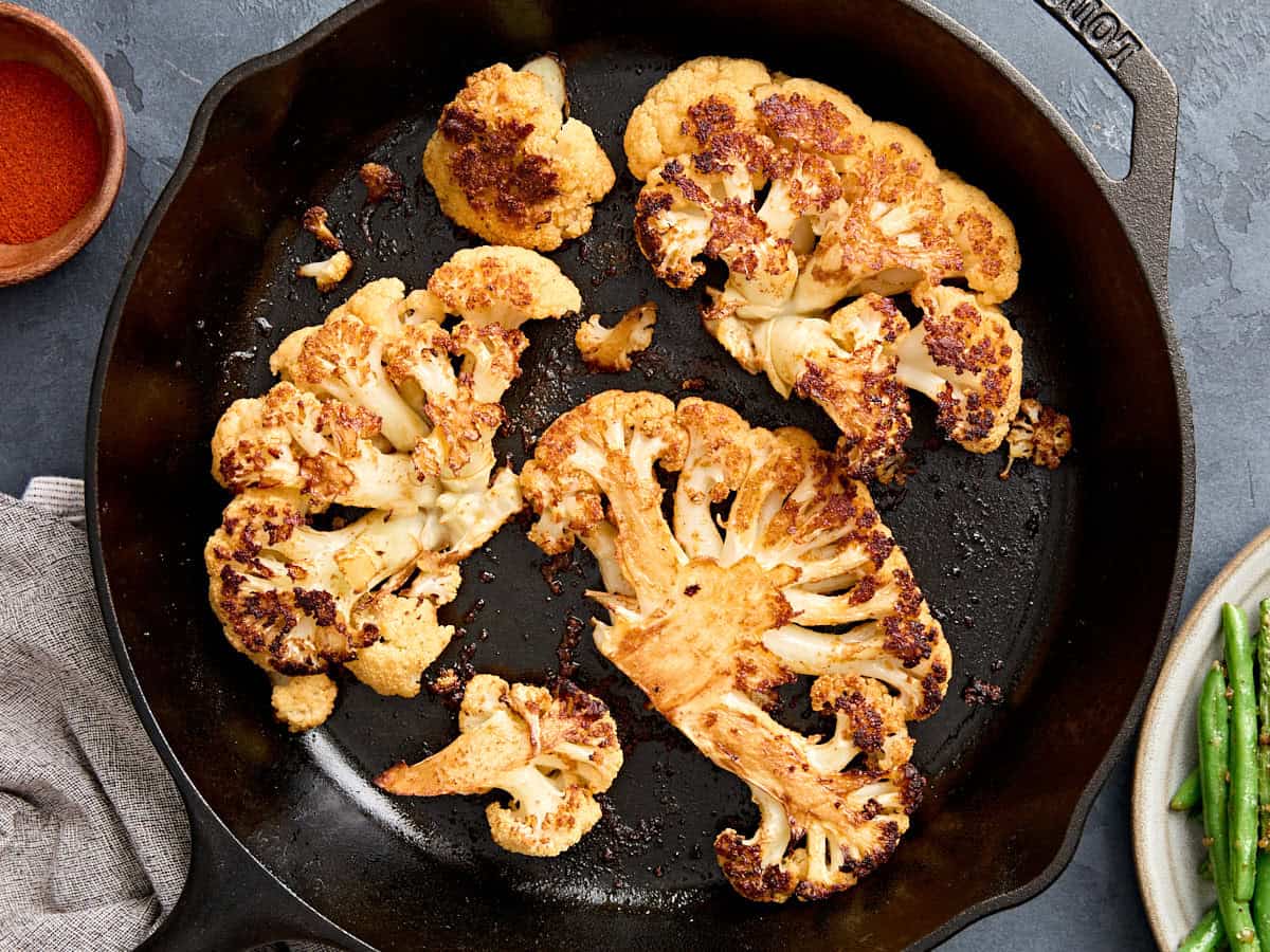 Overhead view of cauliflower steaks in a skillet.