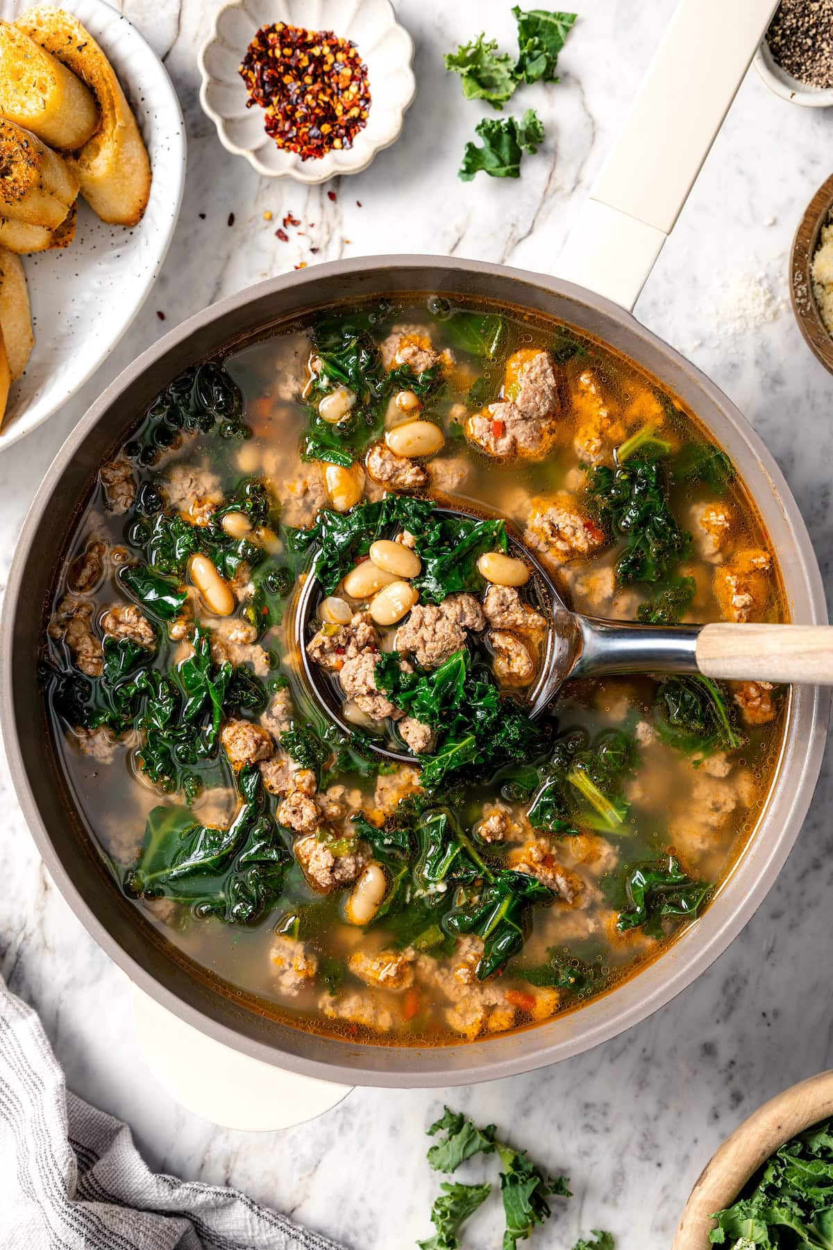 Ladle in pot of white bean soup with sausage and kale.